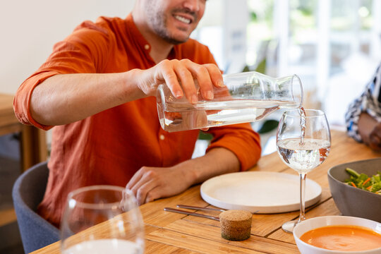 Man pouring water into a glass at a dining table