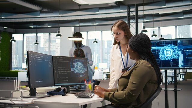 Smiling startup manager teaching junior dev how to use machine learning tech. Happy african american team leader showing intern in office how to use AI predictive models, camera A