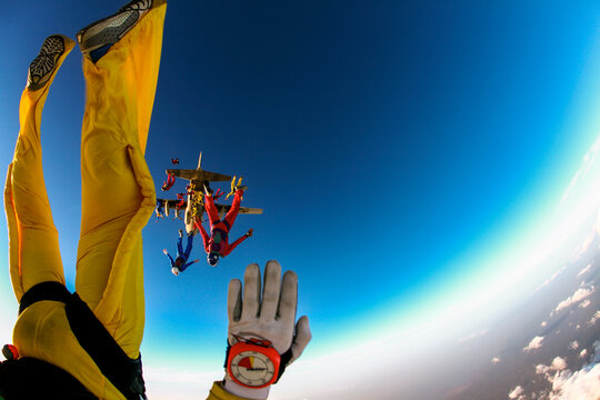 Skydivers exiting aircraft during group jump with strong perspective and copy space. First person view of freefall with colorful parachutists and airplane in background.