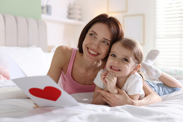 Happy Mother's Day. Little girl greeting her mom with holiday card on bed indoors