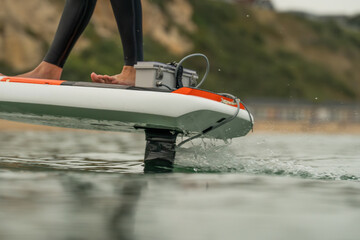 Naklejka premium Close up of an man's feet standing on riding an electric powered hydrofoil surf board, efoil, e-foil, foil drive, hybrid foil.
