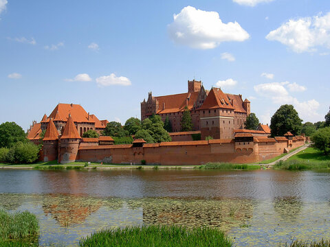 Malbork Castle panorama reflecting in the Nogat river water. Grand medieval brick fortress on a sunny day in Poland.