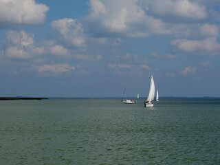 A white sailboat sailing on the lake under a bright, cloudy sky. Recreation and water sports in the Great Masurian Lakes region.