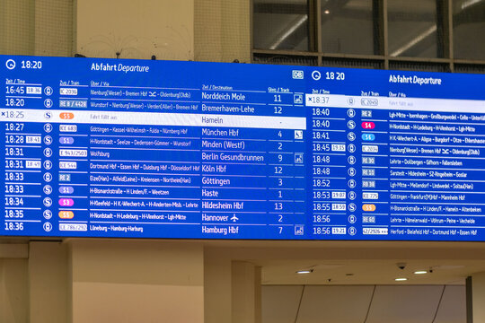 Digital departure board Hannover Hauptbahnhof, displaying train schedules with destinations, DB logo, blue screen interface, Multilingual real-time transit information commuters in Germany, Hannover