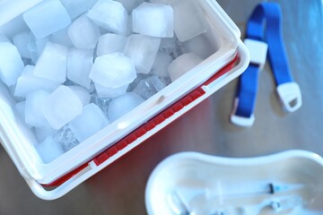 Cool box with ice cubes, medical tourniquet and syringe on table, flat lay