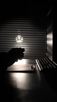 vertical video Hands in silhouette crumpling a sheet of paper at a computer workstation, depicting concepts of stress, frustration, failure, and workplace anger in a dim office environment