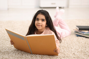 Fototapeta premium Cute little girl reading book on floor at home