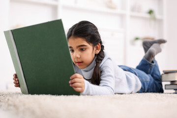 Fototapeta premium Cute little girl reading book on floor at home