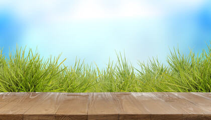 Fototapeta premium Bright green grass and wooden surface against blurred blue background. Banner design