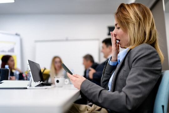 Business meeting with attendees showing interest and distraction in their devices during afternoon session in office setting