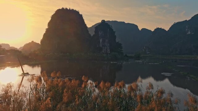 Sunrise in Hang Mua, Ninh Binh, Vietnam, illuminates the Tam Coc rice paddies and towering limestone karsts. The still water reflects the landscape, creating a serene scene.