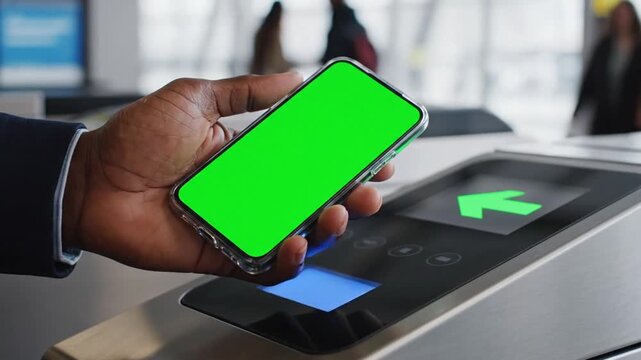 Close-up of a person using a smartphone with a green screen to tap on a contactless payment terminal or access gate.