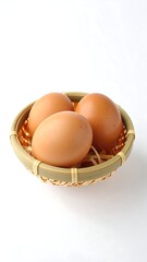 Three brown eggs nestled in a small, round, woven basket with straw on a stark white backdrop