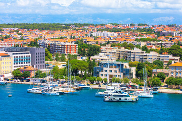 Obraz premium Harbor of Zadar, Croatia, numerous sailboats and yachts are moored in blue waters. Background features a sprawling cityscape of terracotta roofs and modern buildings set against distant mountains
