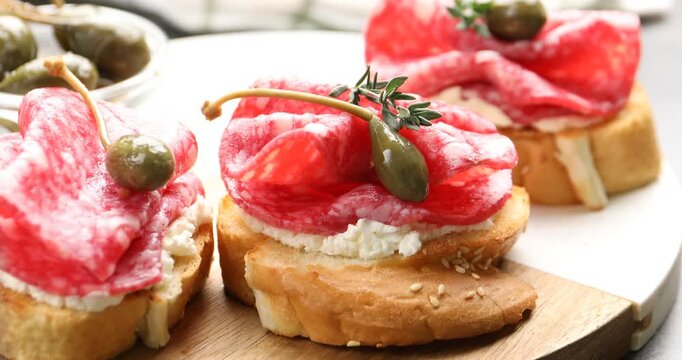 Woman putting thyme sprig onto delicious bruschetta with salami sausage, cream cheese and capers at table, closeup