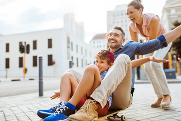 Parents pushing son on skateboard in city street © Geber86