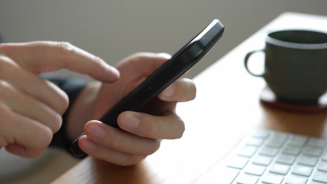 木製のデスクの上で右手で黒いスマートフォンを操作している人