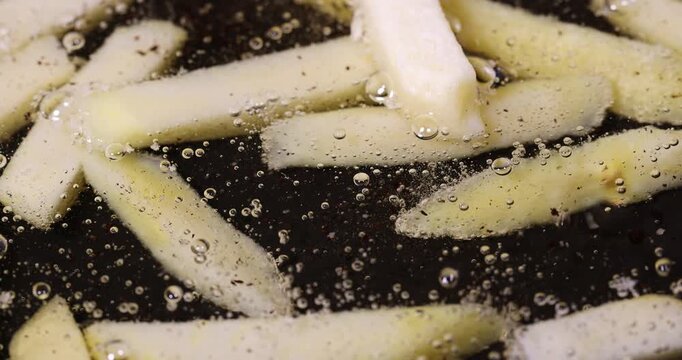 overcooked orange French fries in hot sunflower oil during frying in a frying pan, delicious fast food yellow thawed and fried French fries in hot oil