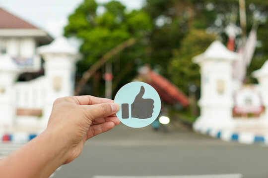 Hand-held humbs Up Sticker icon conveys approval, social media likes and positive feedback. Shot outdoors with shallow depth of field for a clean, modern promotional or marketing concept