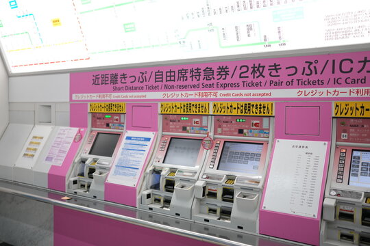 Pink kiosks line station ticketing area. Screens display ticket options for travelers. Modern design suggests efficiency and ease. Bright lighting enhances clean, welcoming feel