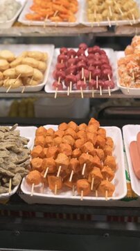 Vertical screen Skewered Fishball Display Street Market Stall, Colorful Trays Of Fried And Grilled Snacks On Foam Platters, Neat Rows Of Orange Meatballs And Assorted Skewers, Vendorready