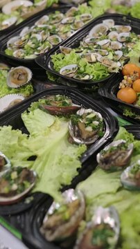 Vertical screen Abalone Trays On Bed Of Lettuce Street Market Seafood Stall Offering Marinated Shellfish, Citrus Garnish, Herbs, Tidy Black Trays And Closeup Fresh Details