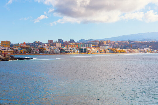 Expansive Las Canteras Beach in Las Palmas de Gran Canaria, Spain, showing city skyline along water's edge. Calm Atlantic Ocean Leading to a long stretch of urban coastline and distant mountains