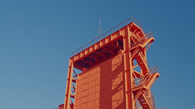 A detailed side view of the historic Red Iwabuchi Sluice Gate's tower, highlighting its industrial steel staircase against a clear blue sky.