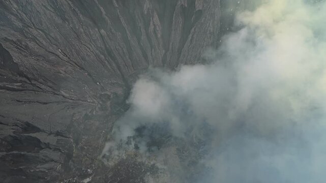 Stunning top down aerial view of the active crater of mount bromo volcano. Sulfuric smoke and gas are rising from its caldera in indonesia
