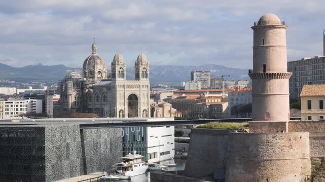 Telephoto view compressing Marseille's iconic landmarks: MuCEM, Cath&eacute;drale La Major and the Fanal Tower together under a bright cloudy sky.