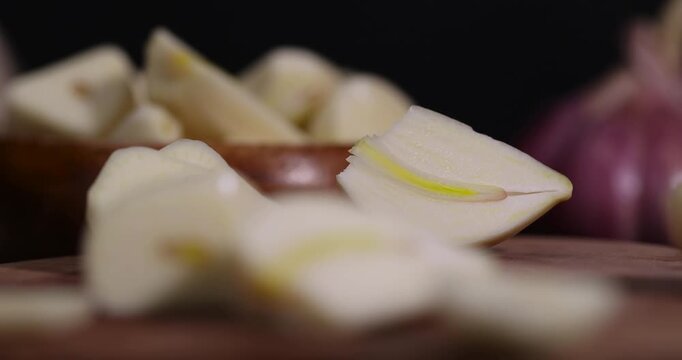 peeled and sliced purple garlic scattered on the black table and peeled and sliced, fragrant fresh and natural garlic spices scattered on the kitchen table during cooking