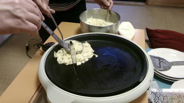 Cooking Japanese Okonomiyaki Savory Pancake on a Hot Griddle. Chef preparing traditional Osaka-style okonomiyaki with fresh cabbage batter on a flat iron griddle at a street food market.