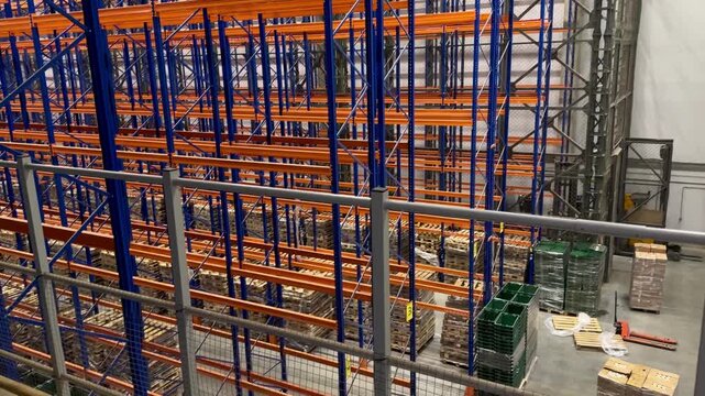 High angle view of a large warehouse with tall blue pallet racking systems. Industrial logistics facility featuring organized storage zones, numbered aisles and goods ready for distribution.