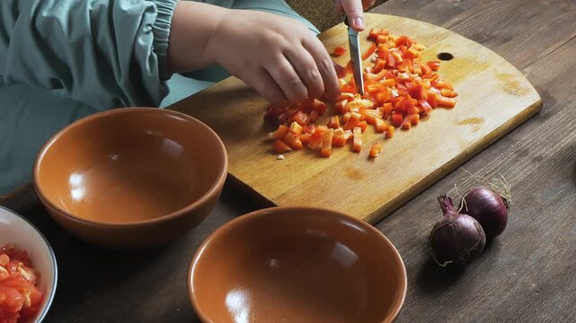 Red peppers are sliced with a knife on a cutting board on the table and placed on a plate