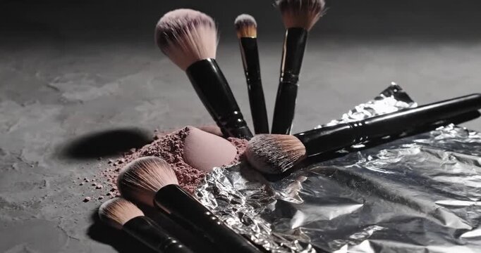 A collection of makeup brushes scattered around crushed powder on a reflective surface
