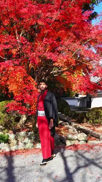 Man wearing kimono walking under red autumn tree in Kyoto Japan