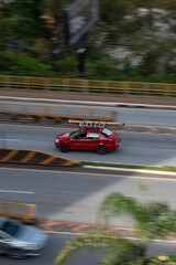 Naklejka premium Red Fiat Siena side profile in motion, Compact work sedan driving on city avenue