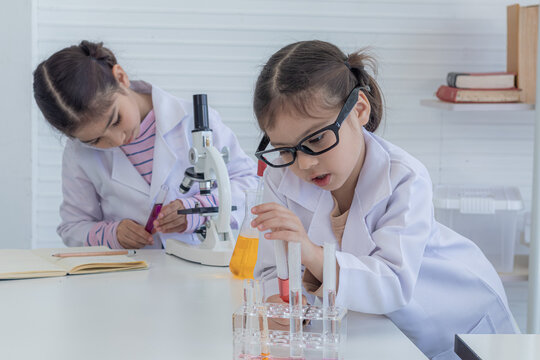 Group of sibling primary school students wearing lab coats having fun play dropping equipment liquid substance in glass flask in laboratory classroom, lifestyle learning education science class