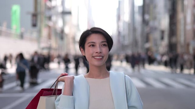 ショッピングバッグを持って銀座の通りを楽しそうに歩く女性のトラッキングショット
