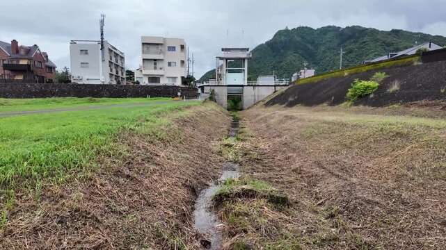 Drainage canal near Mt. Kinka in Gifu City, Japan, features a sluice gate to prevent backflow and regulate water levels serving as infrastructure for urban rainwater runoff management