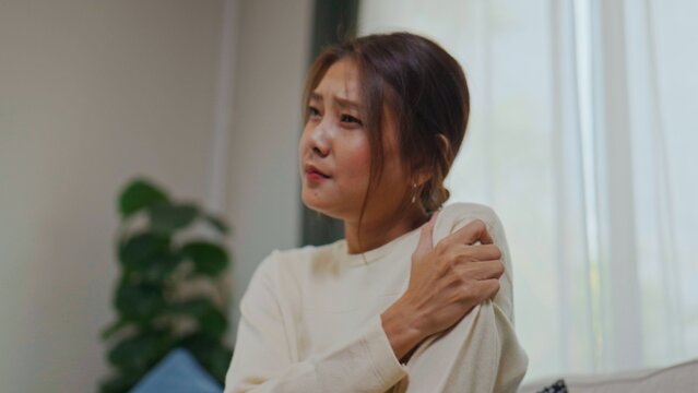 Asian woman suffering from shoulder pain on sofa