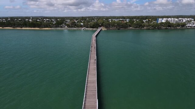 Aerial view of the historic Urangan Pier and foreshore located in the coastal town of Hervey Bay Queensland Australia. Moving drone view