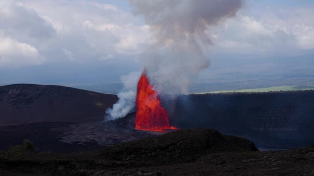 4K slow motion footage of Kīlauea eruption framed by foreground vegetation, with lava effusion and rising smoke visible beyond crater rim.