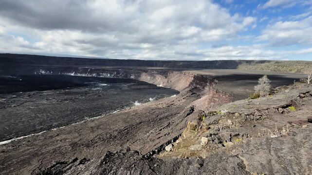 Static 4K wide shot of Kīlauea caldera showing vast basalt terrain and light fumaroles rising gently from the volcanic crater floor.