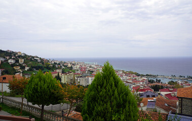 Obraz premium An elevated view looks out over the red-tiled roofs of houses toward a coastal city and the Black Sea under an overcast sky in Trabzon, Turkey