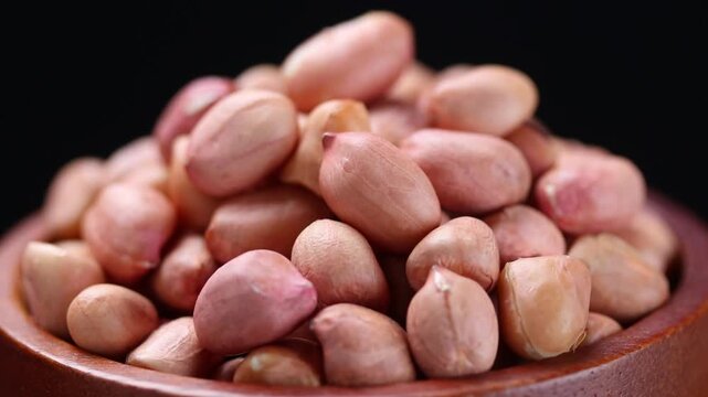 Pile of raw peanuts in a wooden bowl rotating slowly on a black background.