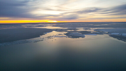 Fototapeta premium Aerial Frozen Lake Dotted With Islands, Ecologist Mapping Island Habitats And Shoreline Ice, Scattered Dark Islets Contrast With Smooth Ice Sheets, Low Winter Light And Clear Coastal Geometry.