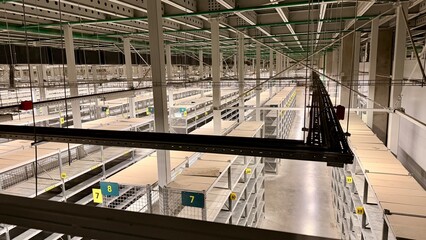 Fototapeta premium High angle view of large industrial warehouse with long rows of metal mesh shelves and numbered sections. Modern logistics distribution center interior for storage and inventory management.