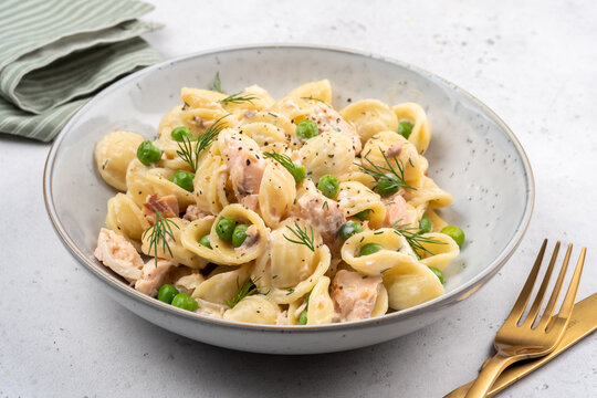 Pasta with chicken and peas on a white plate served for lunch on a table with golden fork