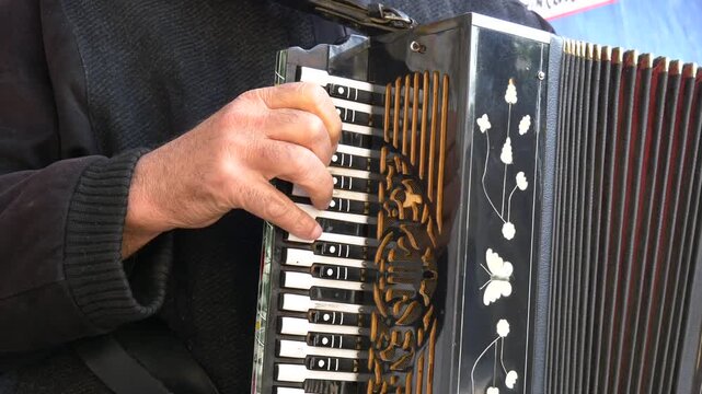 Street musician playing traditional accordion with ornate butterfly decorations on sunny outdoor day